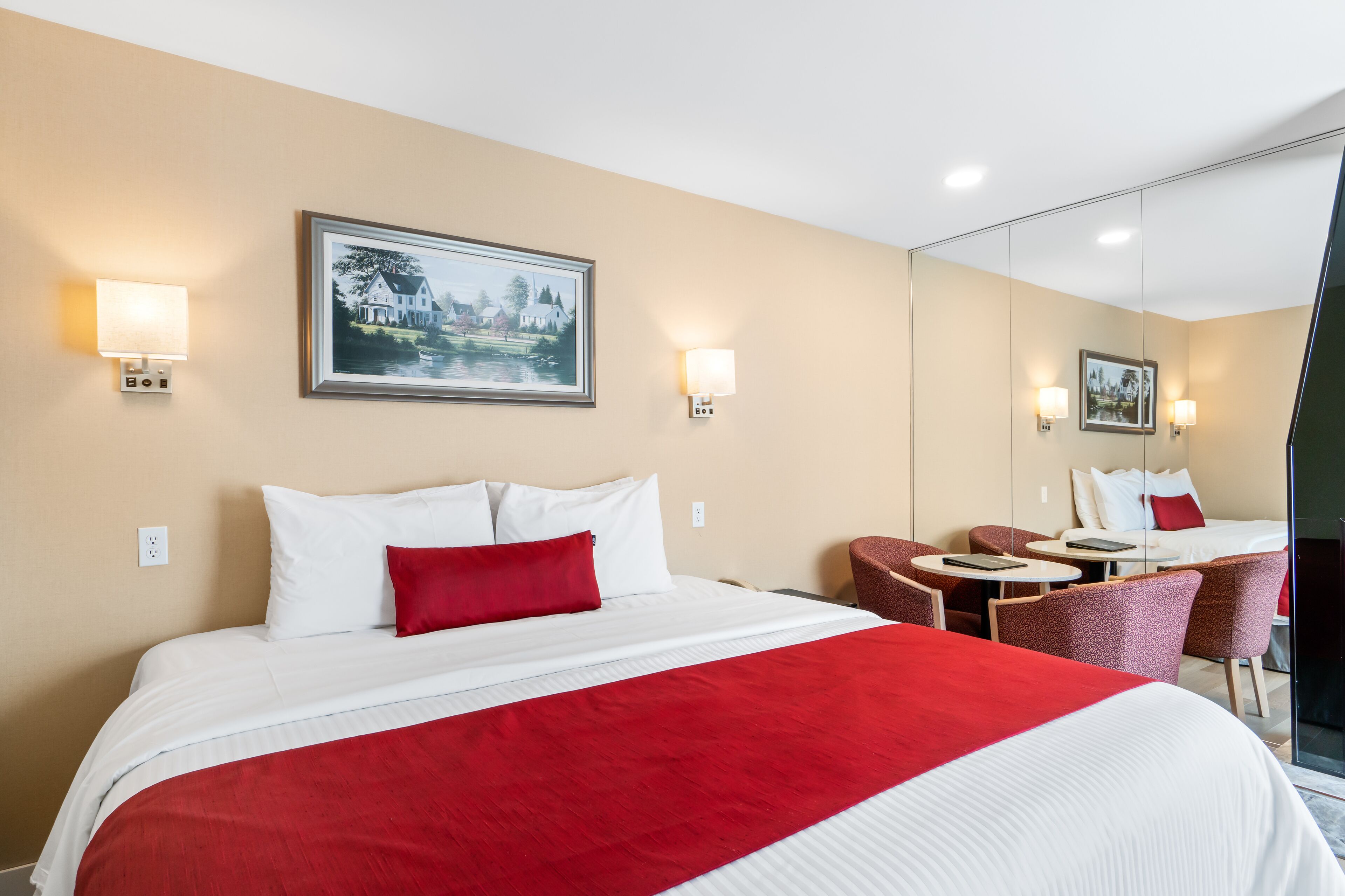 Habitación de hotel con una cama grande, un escritorio y una silla. Hay dos lámparas de pared y un cuadro en la pared.