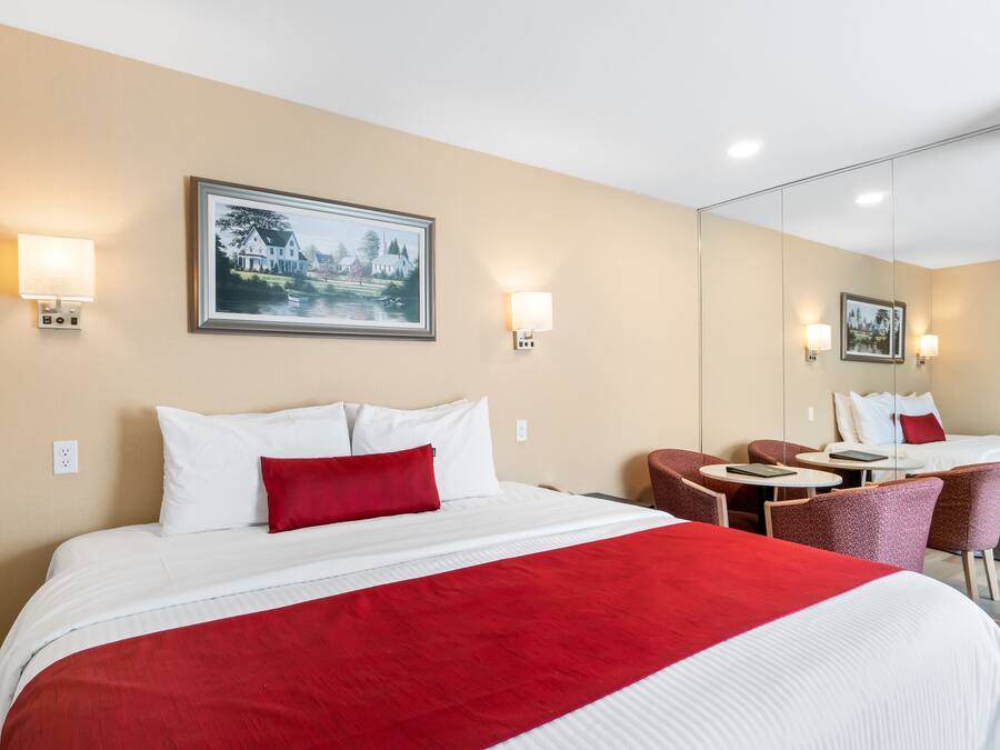 Habitación de hotel con una cama grande, un escritorio y una silla. Hay dos lámparas de pared y un cuadro en la pared.