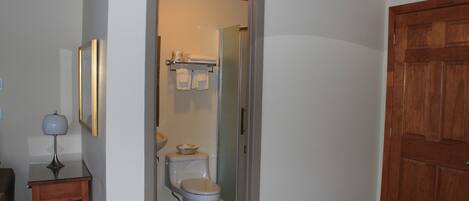 A bathroom with a toilet, a small table with a lamp, and a wooden door.