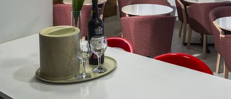 A restaurant interior with round tables and chairs, a wooden accent wall, and a large window.