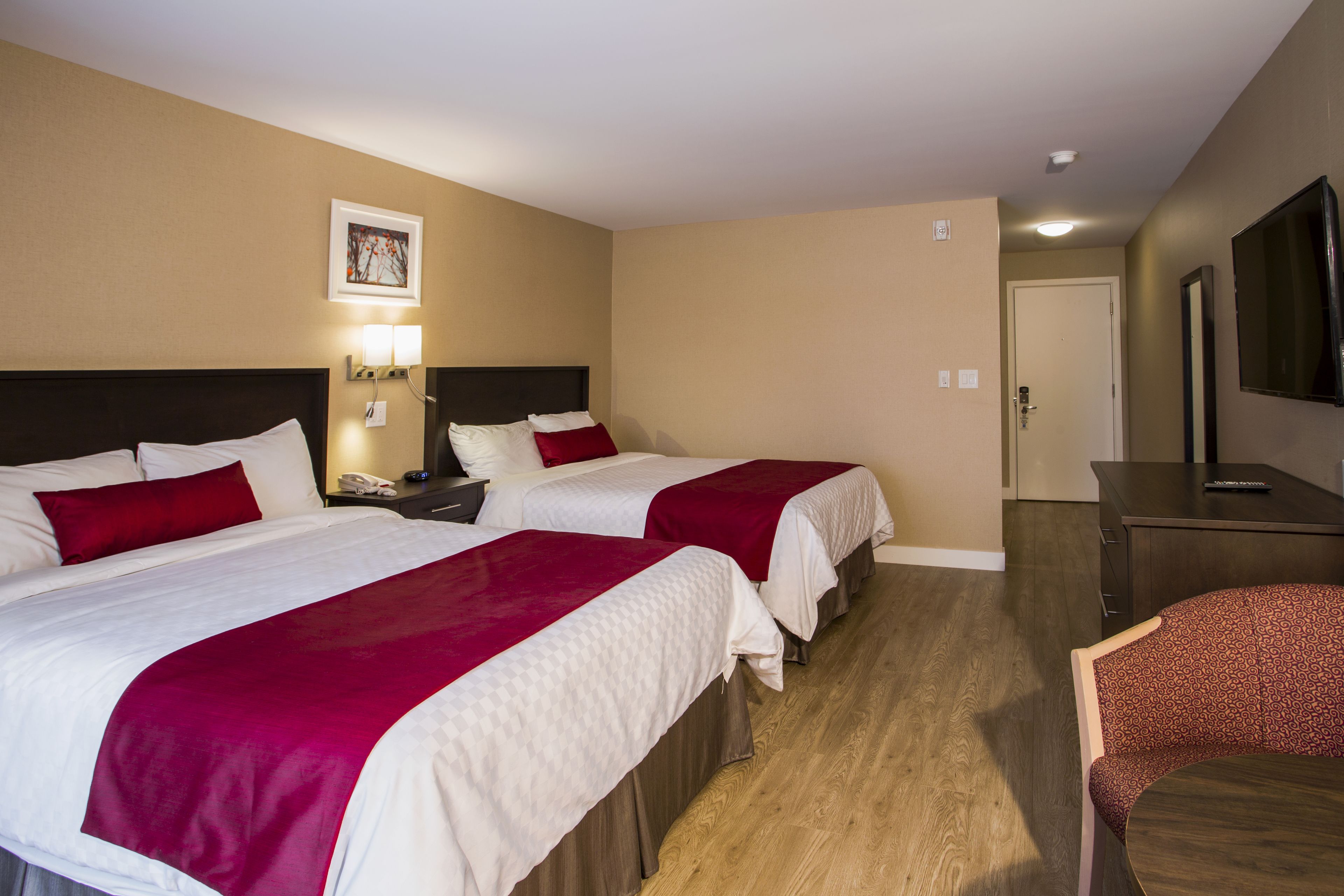 A hotel room with two beds, a desk, a chair, and a TV.