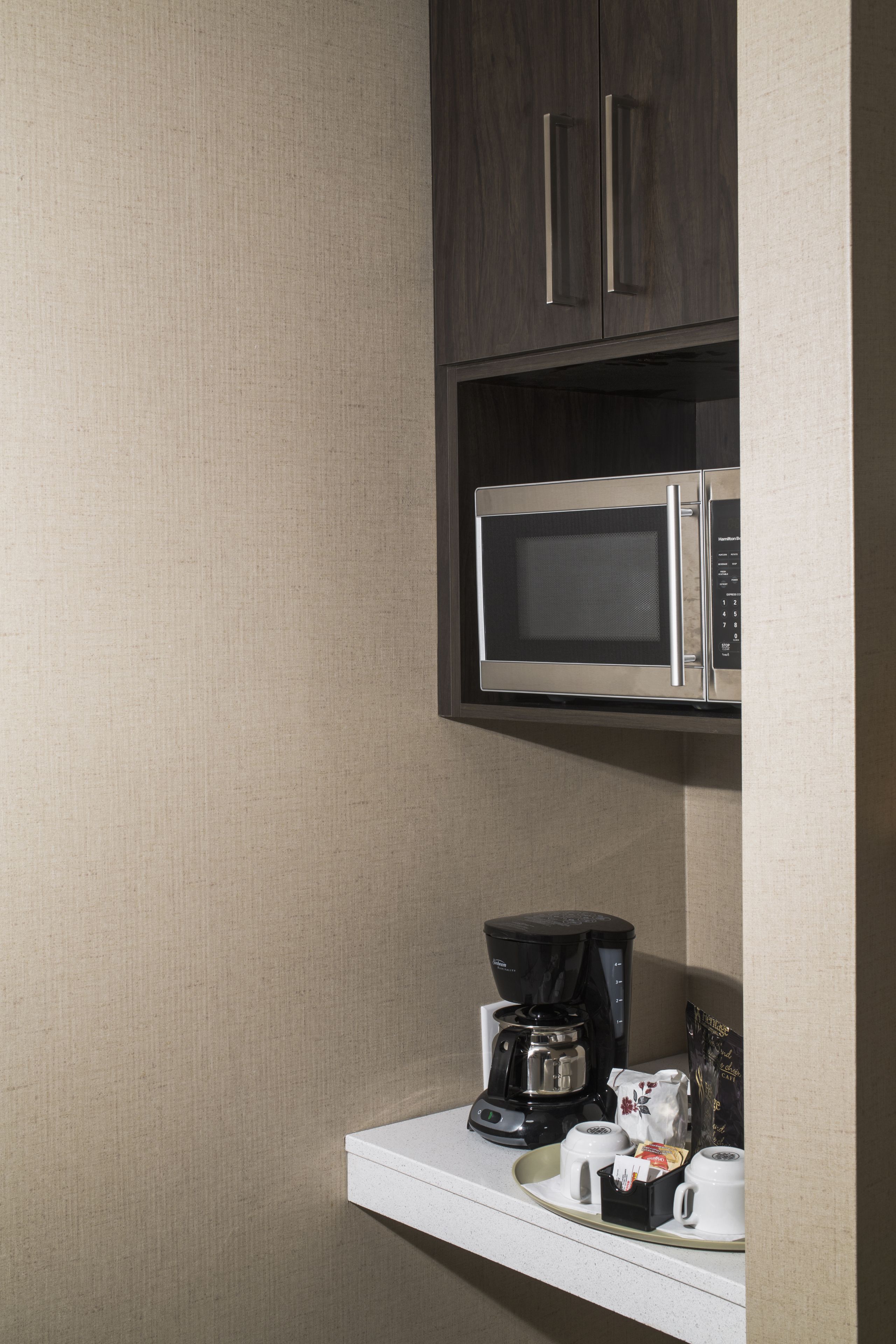 Een kitchenette met een magnetron, koffiezetapparaat en een dienblad met bekers en een doos.