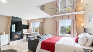 A modern hotel room with a fireplace, a bed with white and red bedding, a sofa, and a desk with a chair. - Hotel Bromont (Bromont)