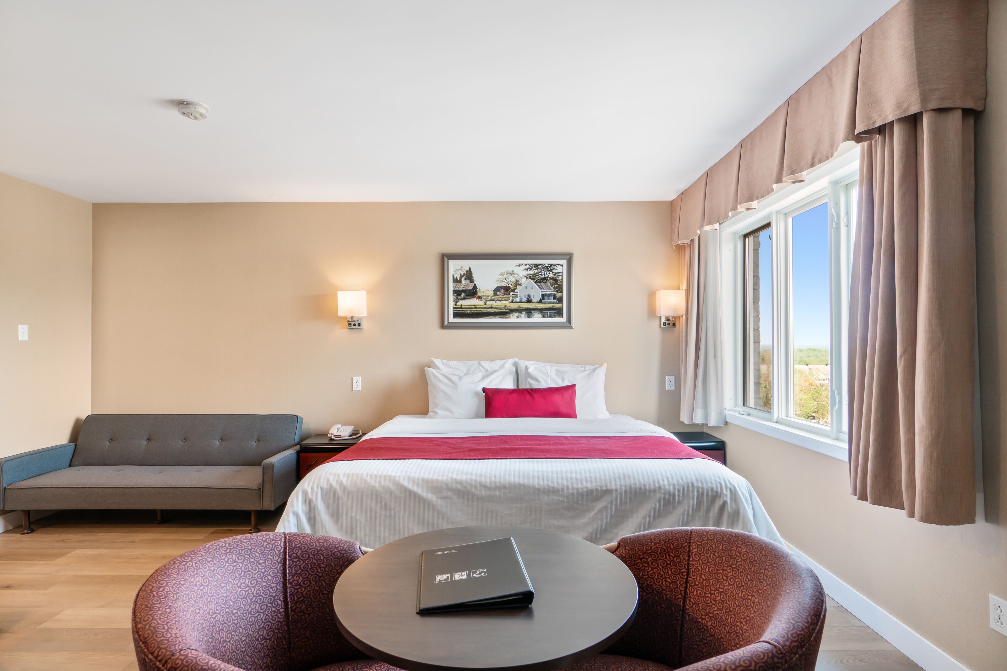 A hotel room with a bed, a sofa, a dining table, and a window with curtains.