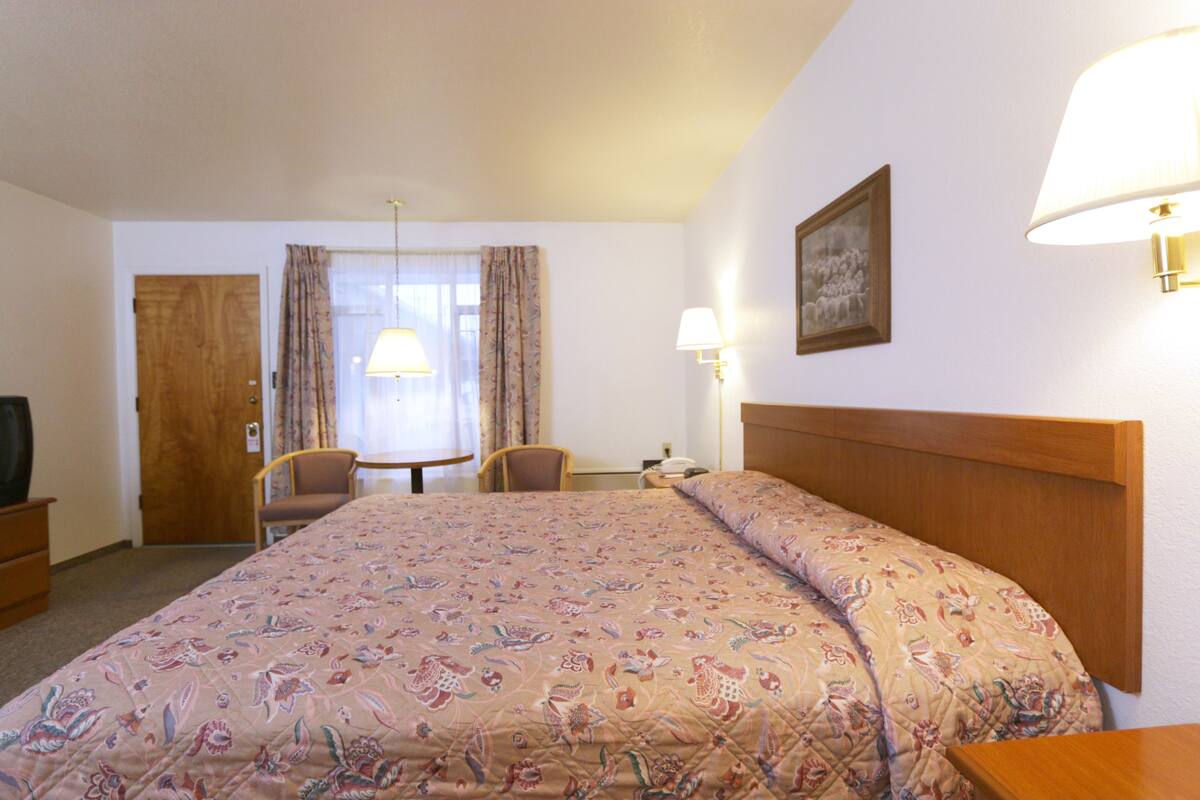 Una habitación de hotel con una cama grande, dos sillones, una mesita, un televisor y una lámpara.