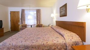 A hotel room with a large bed, two chairs, a small table, a television, and a lamp. - Town House Motel (Winnemucca)
