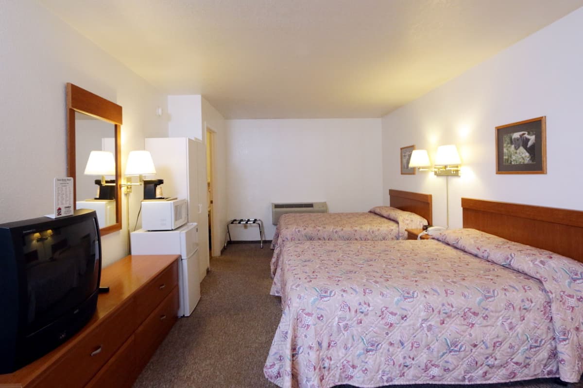 Habitación de hotel con dos camas, televisión, escritorio, espejo y dos lámparas fijadas a la pared.