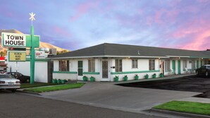 A motel with a green and white exterior, a parking lot, and a mountain in the background. - Town House Motel (Winnemucca)