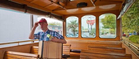 A vintage bus interior with wooden benches, a man sitting with a suitcase, and a view of a road through the windows.
