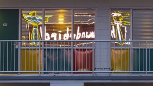 Fachada de edificio con tres ventanas, arte de neón y barandilla de balcón.