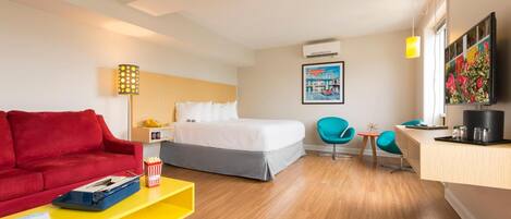A hotel room with a bed, a red couch, a yellow coffee table, a desk with a chair, and a TV on the wall.