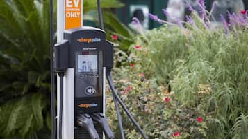 An EV charging station with a digital display, charging cables, and a yellow pipe.