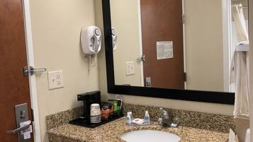 A hotel bathroom with a granite countertop sink, a large mirror, a hairdryer, and a towel rack.