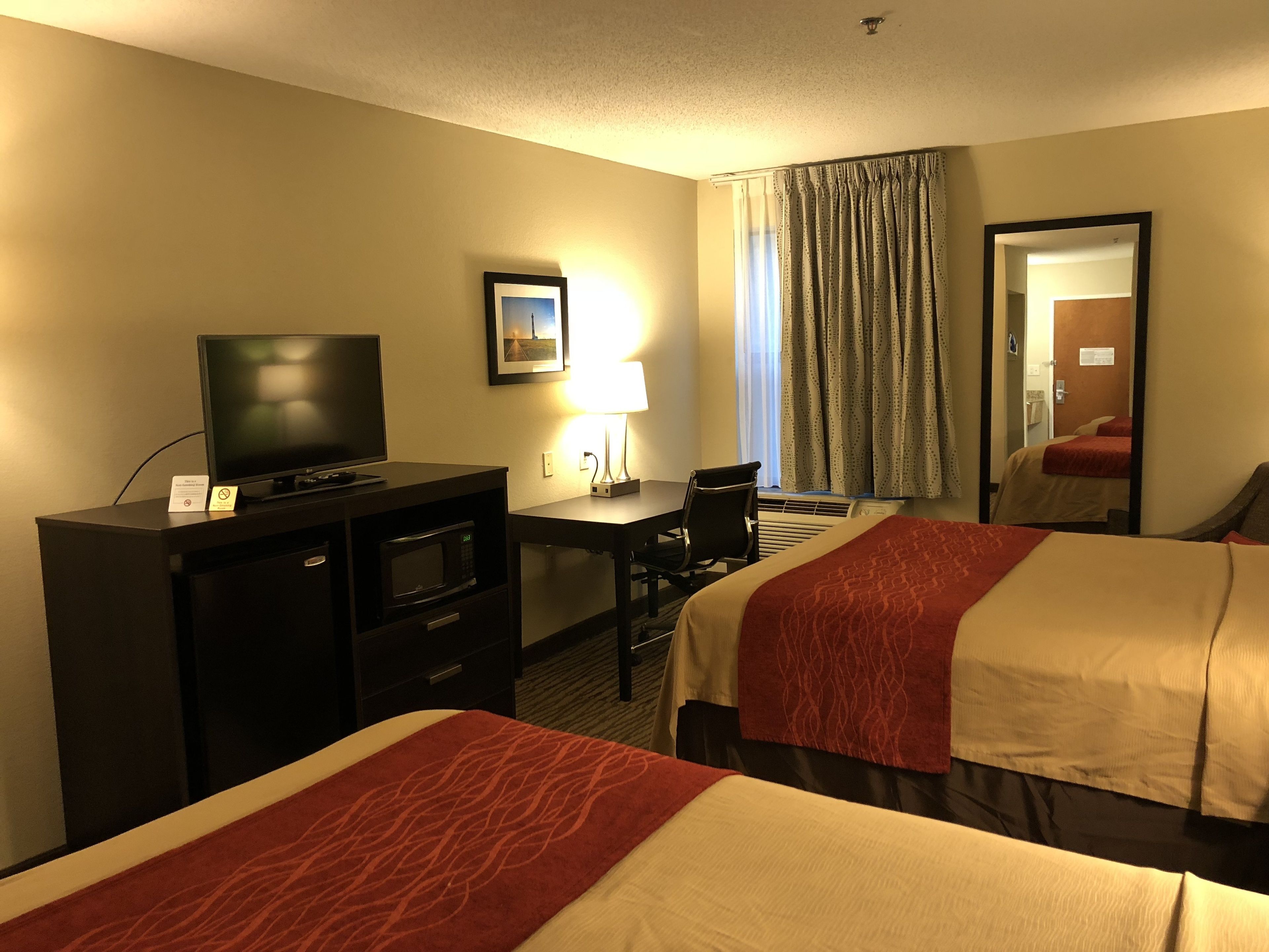 Habitación de hotel con dos camas, un escritorio, un televisor, una silla, una lámpara y un espejo.