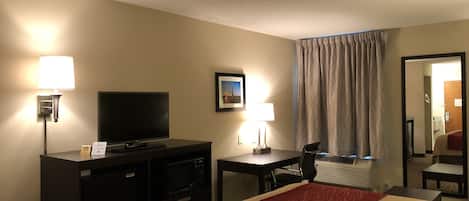 A hotel room with a bed, a TV, a desk, a lamp, and a picture on the wall.