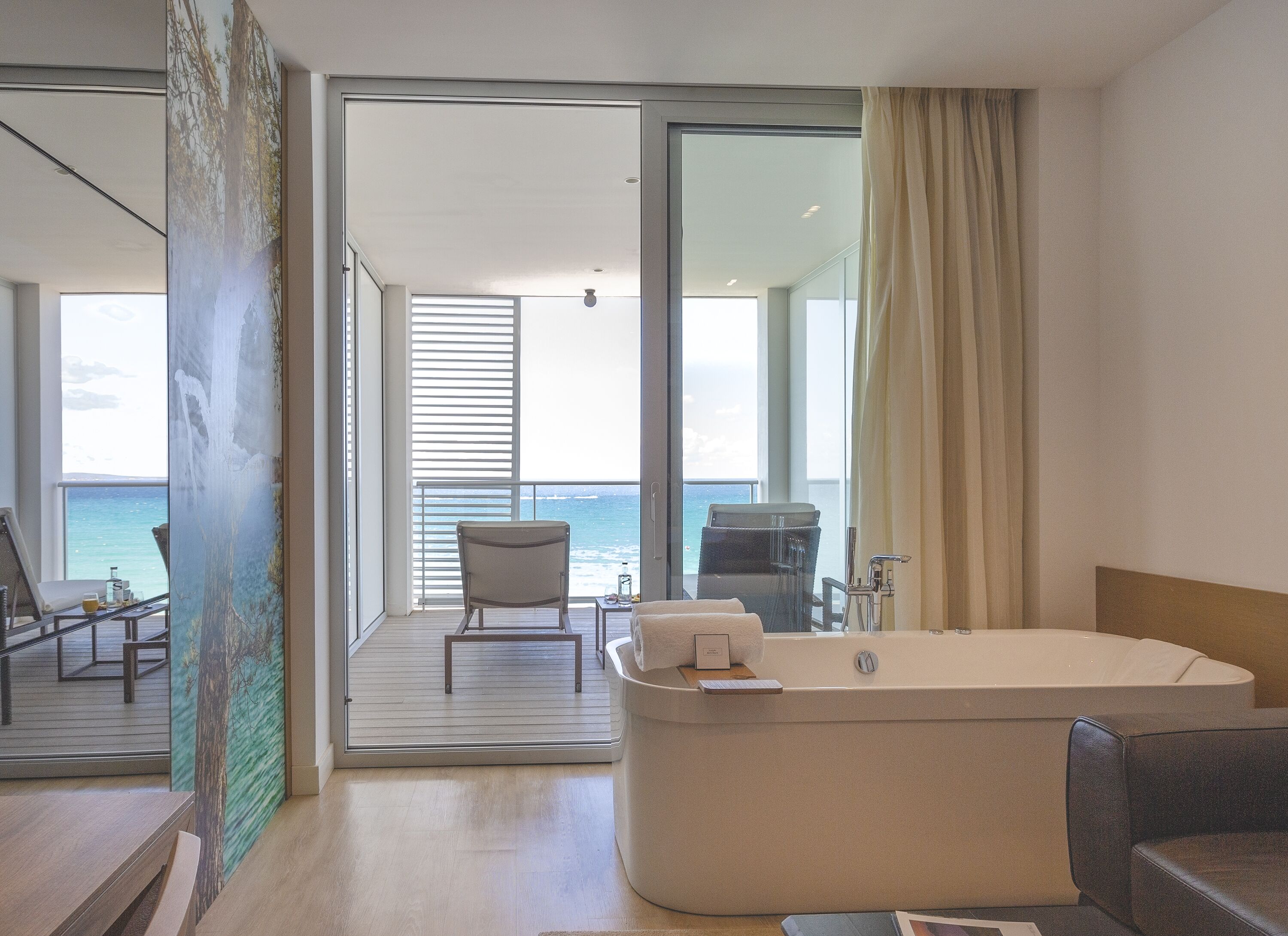 Ein modernes Badezimmer mit einer großen Badewanne, einer Sitzecke mit Meerblick und einem Balkon mit einem Sessel.