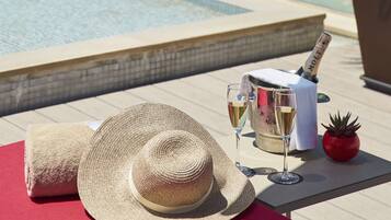 A poolside setting with a clear view of the ocean, a bottle of champagne, and a straw hat on a red mat.