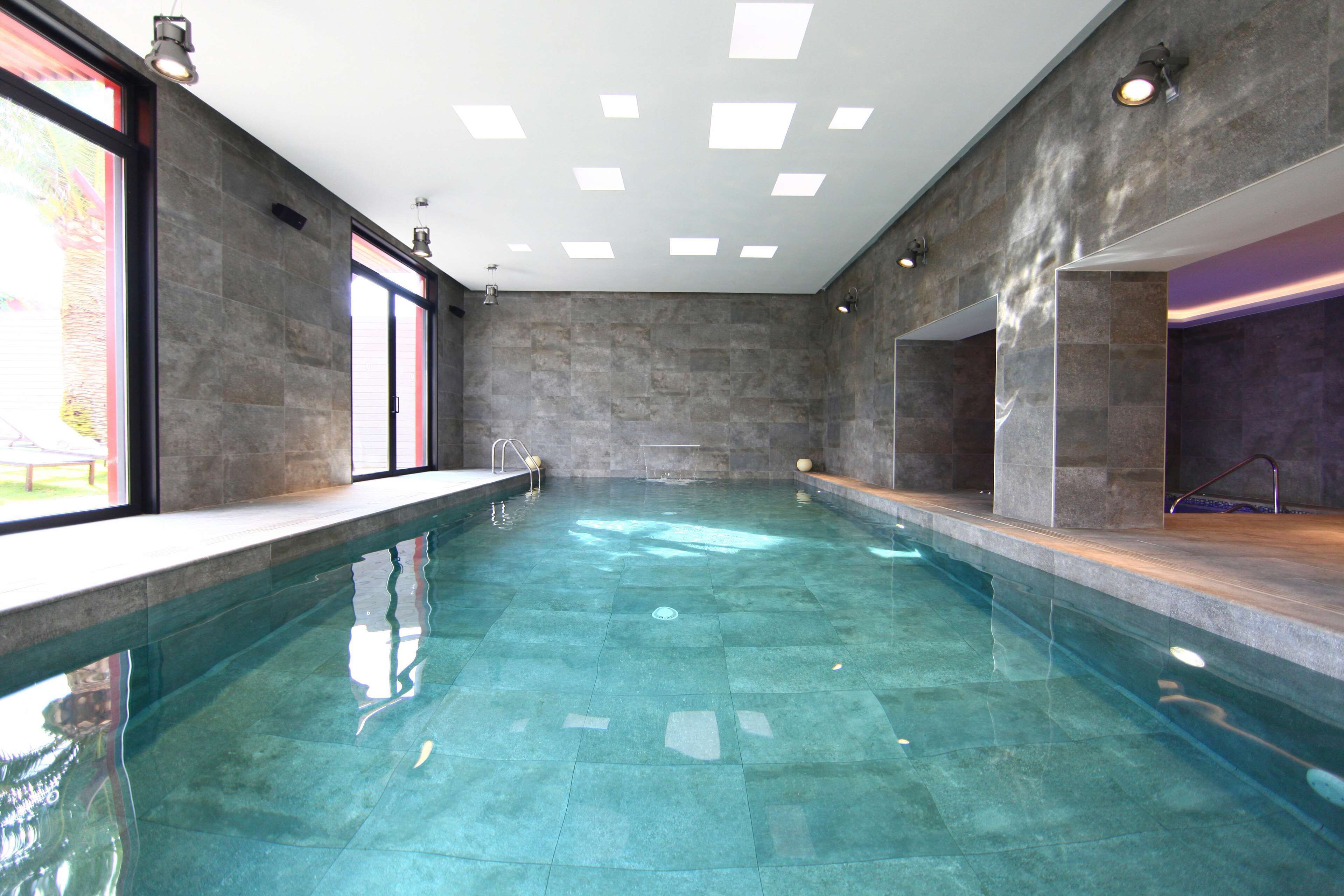 Una piscina interior con agua cristalina, rodeada de muros de piedra y amplias ventanas.