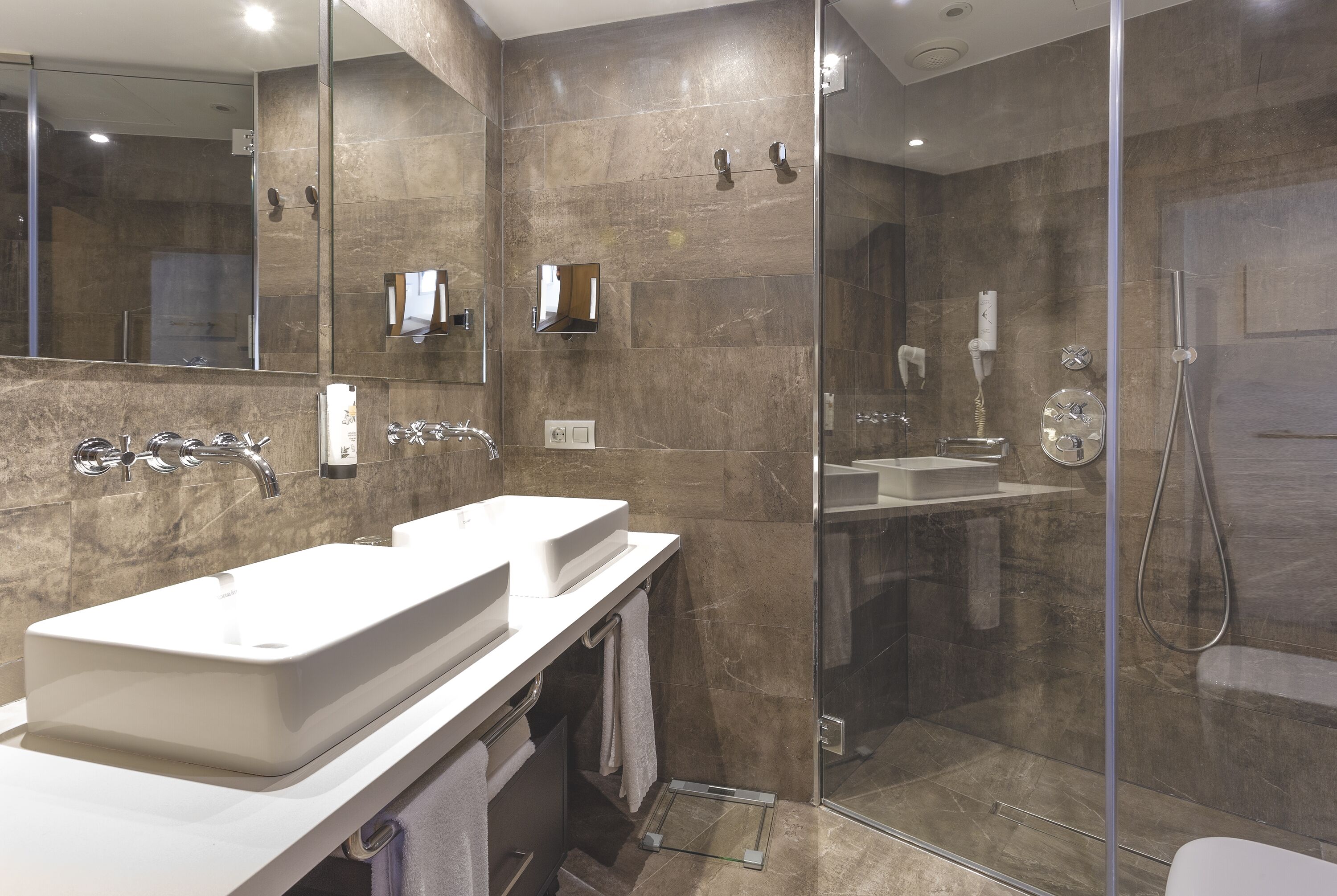 A modern bathroom with two sinks, a glass shower enclosure, and a large mirror.