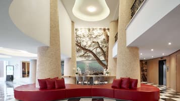 A modern lobby with a curved red seating area, a large tree mural, and a checkered floor.