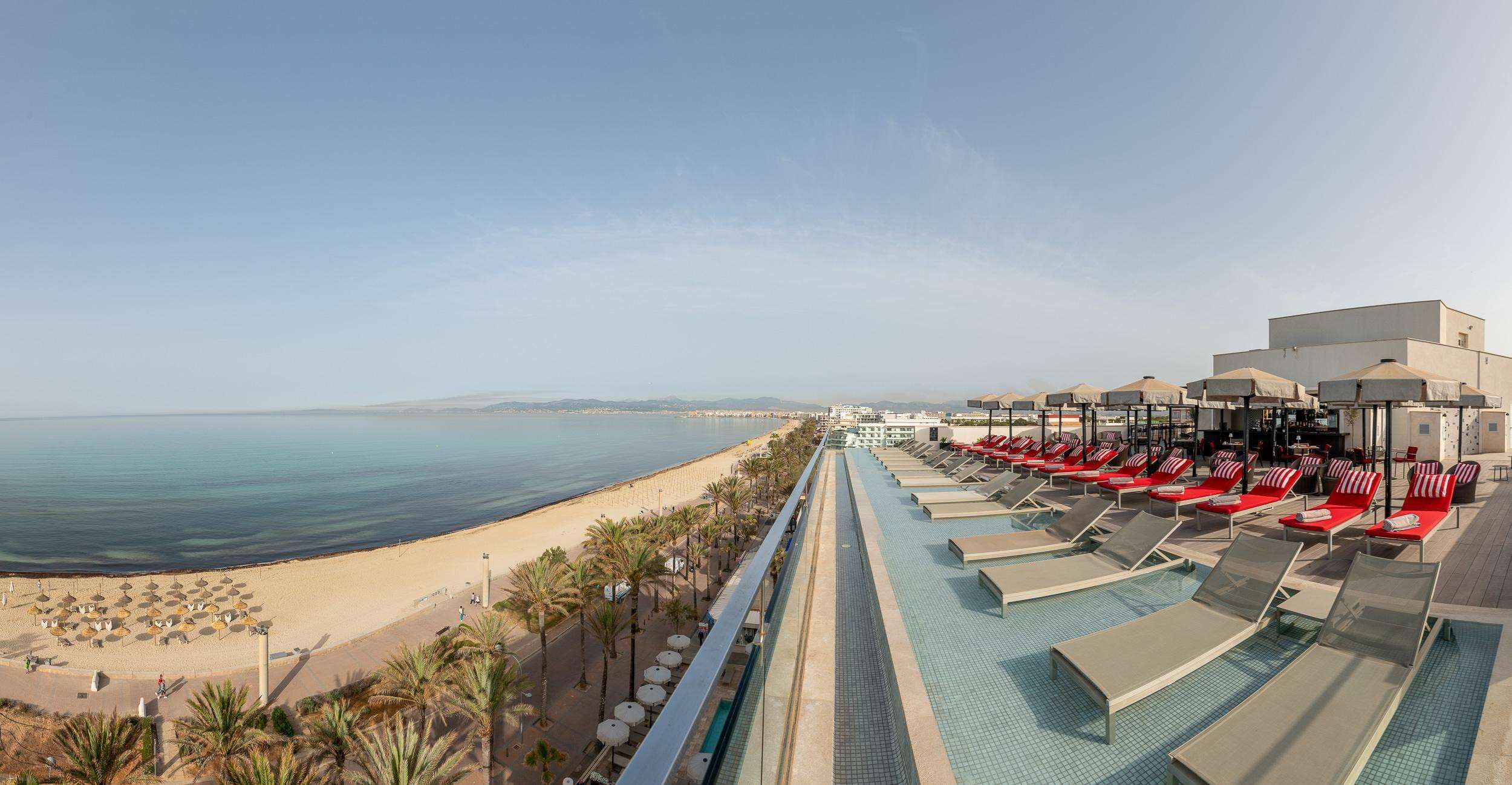 Piscina de un complejo turístico con tumbonas y vista a la playa.