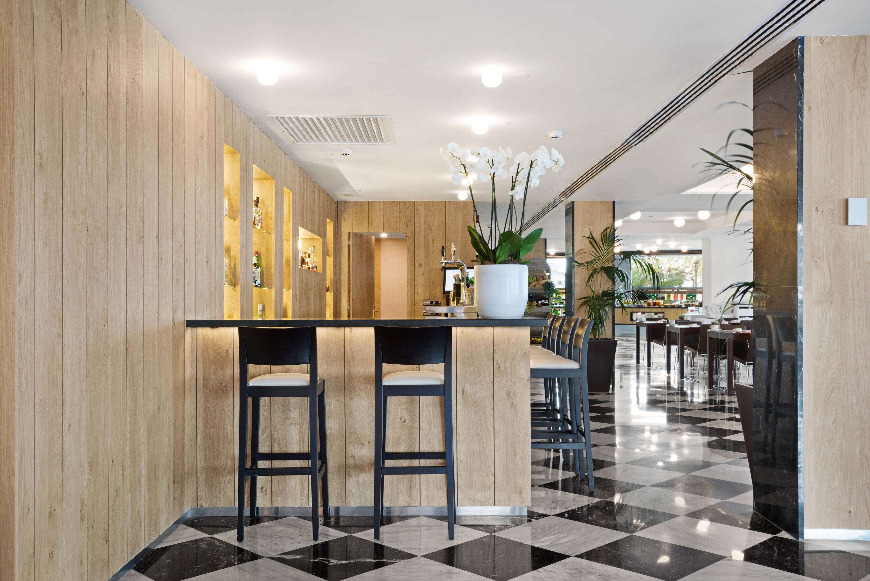 Eine moderne Hotelhalle mit einem hölzernen Empfangstresen, einem schwarz-weißen Schachbrettboden und einer großen Topfpflanze.
