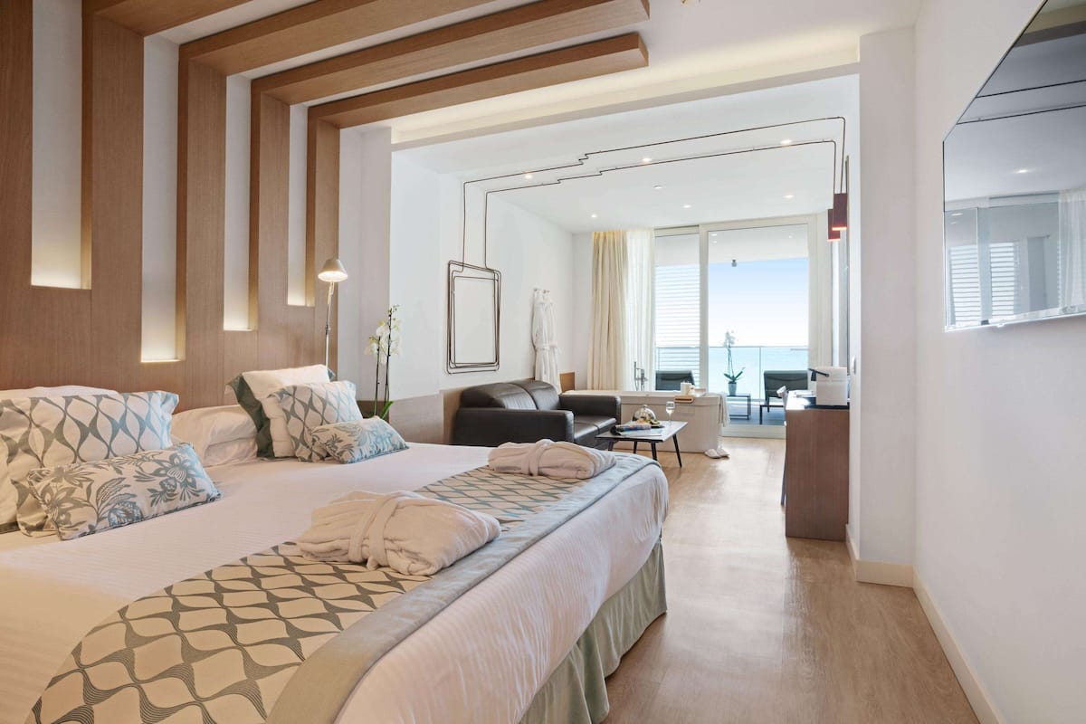 A modern hotel room with a large bed, a sofa, a desk, and a view of the balcony.