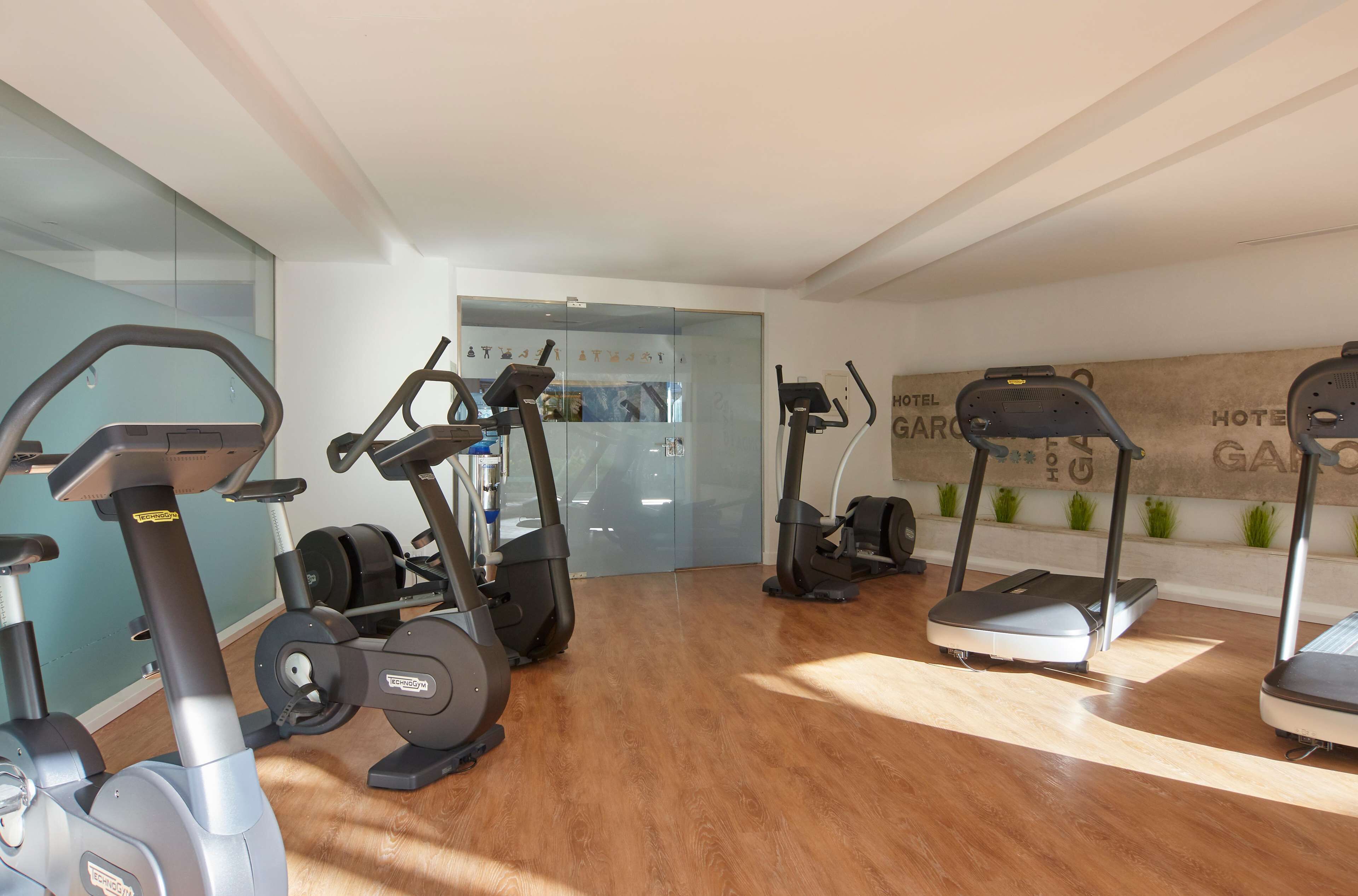 Gimnasio de hotel con diversos equipos de ejercicio, incluyendo cintas de correr y bicicletas estáticas.