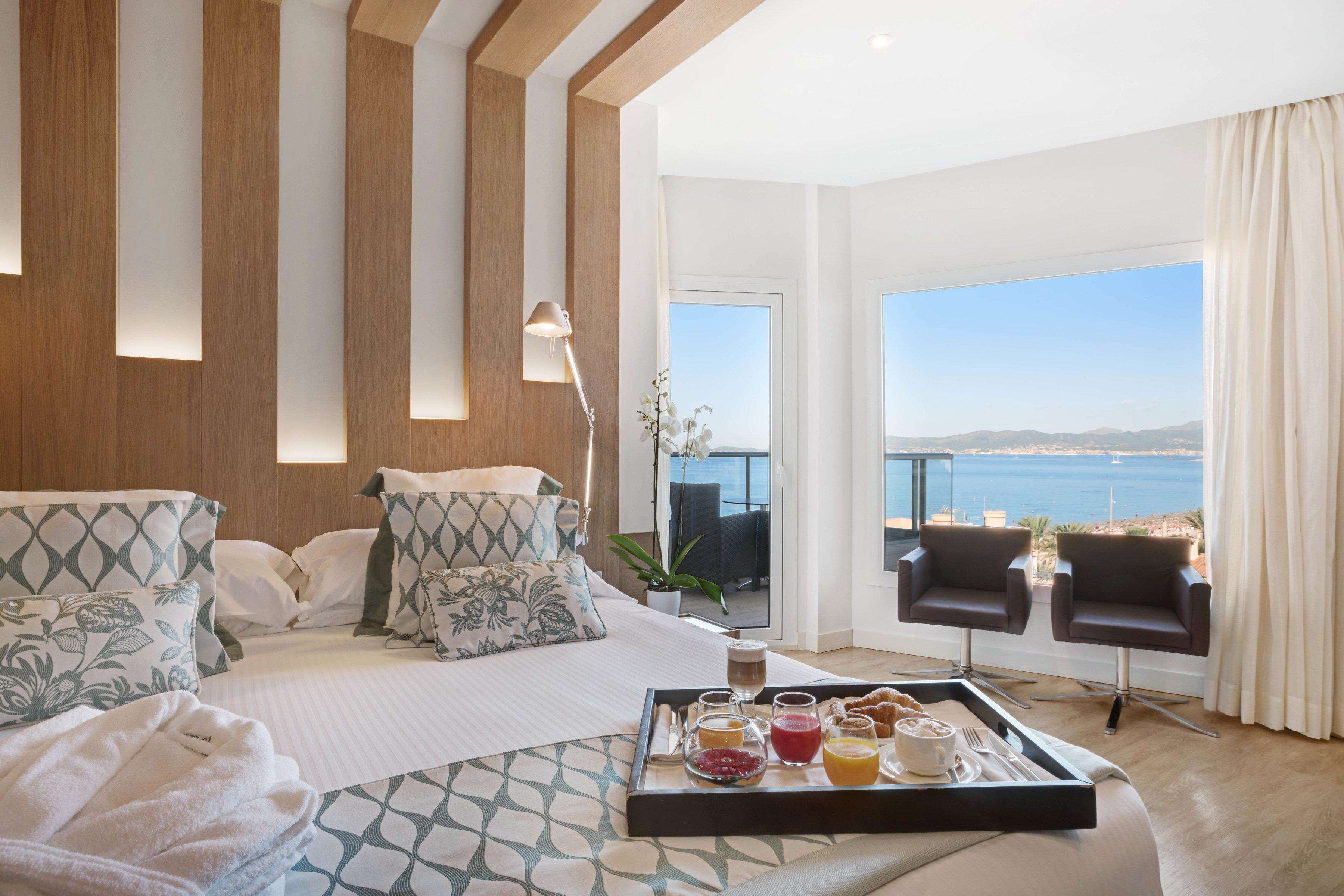 A hotel room with a bed, a breakfast tray, and a view of the sea.