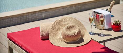 Escena junto a la piscina con una silla de descanso roja, un sombrero de paja, copas de champán y una botella de champán.
