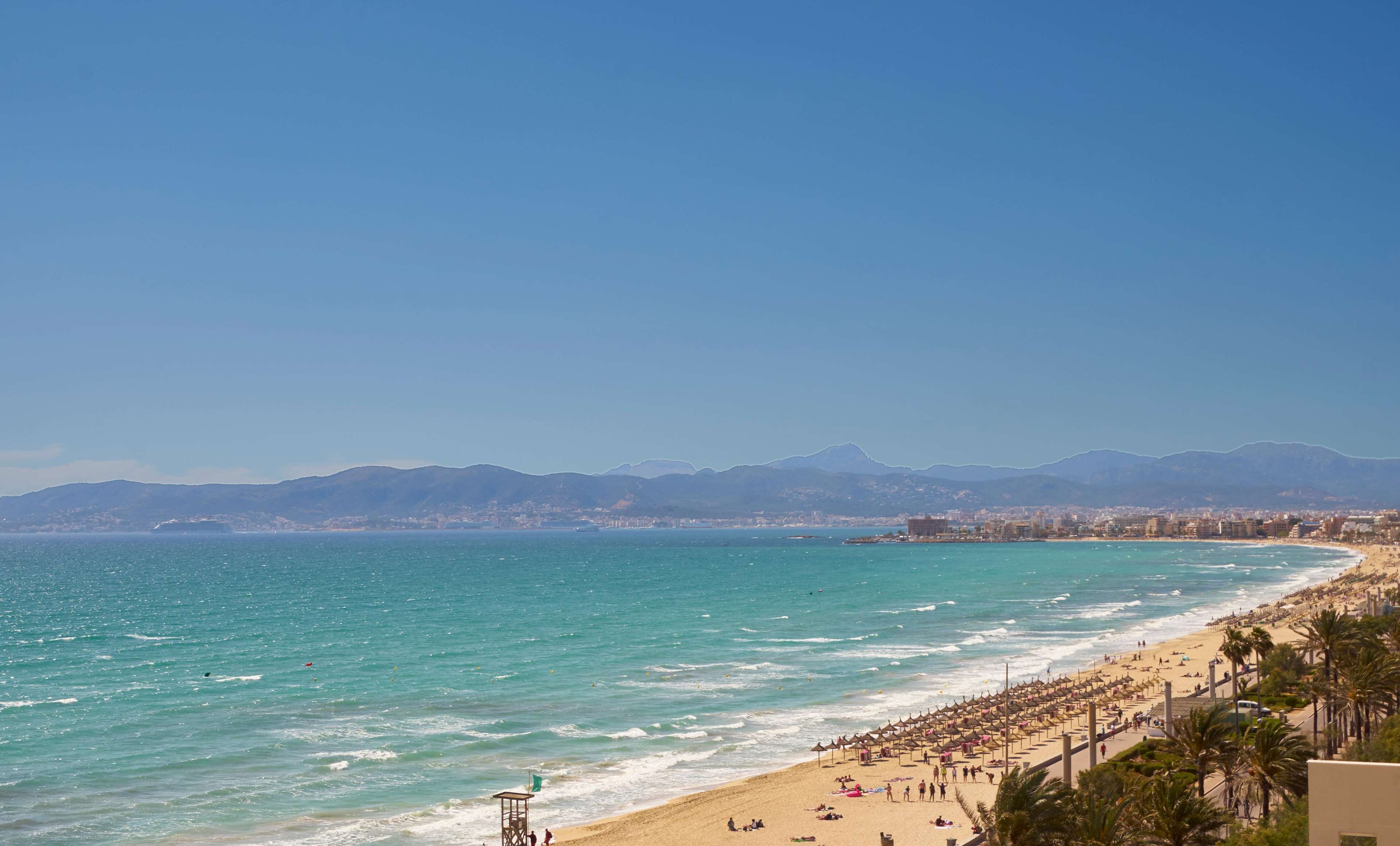 Una playa con una torre de salvavidas, sombrillas y gente.