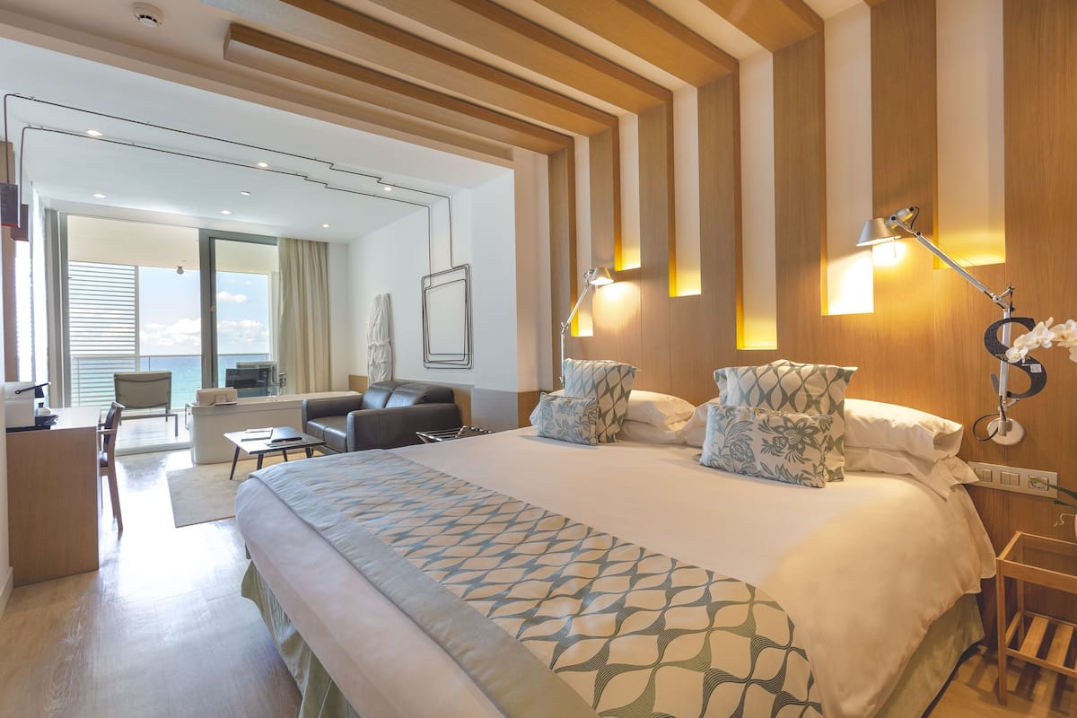 A modern hotel room with a large bed, a desk, a chair, and a view of the ocean.