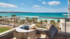 A balcony with a view of the ocean, a table with a bottle, glasses, and a hat, and a wicker chair. - Pure Salt Garonda - Adults Only (Palma de Mallorca)