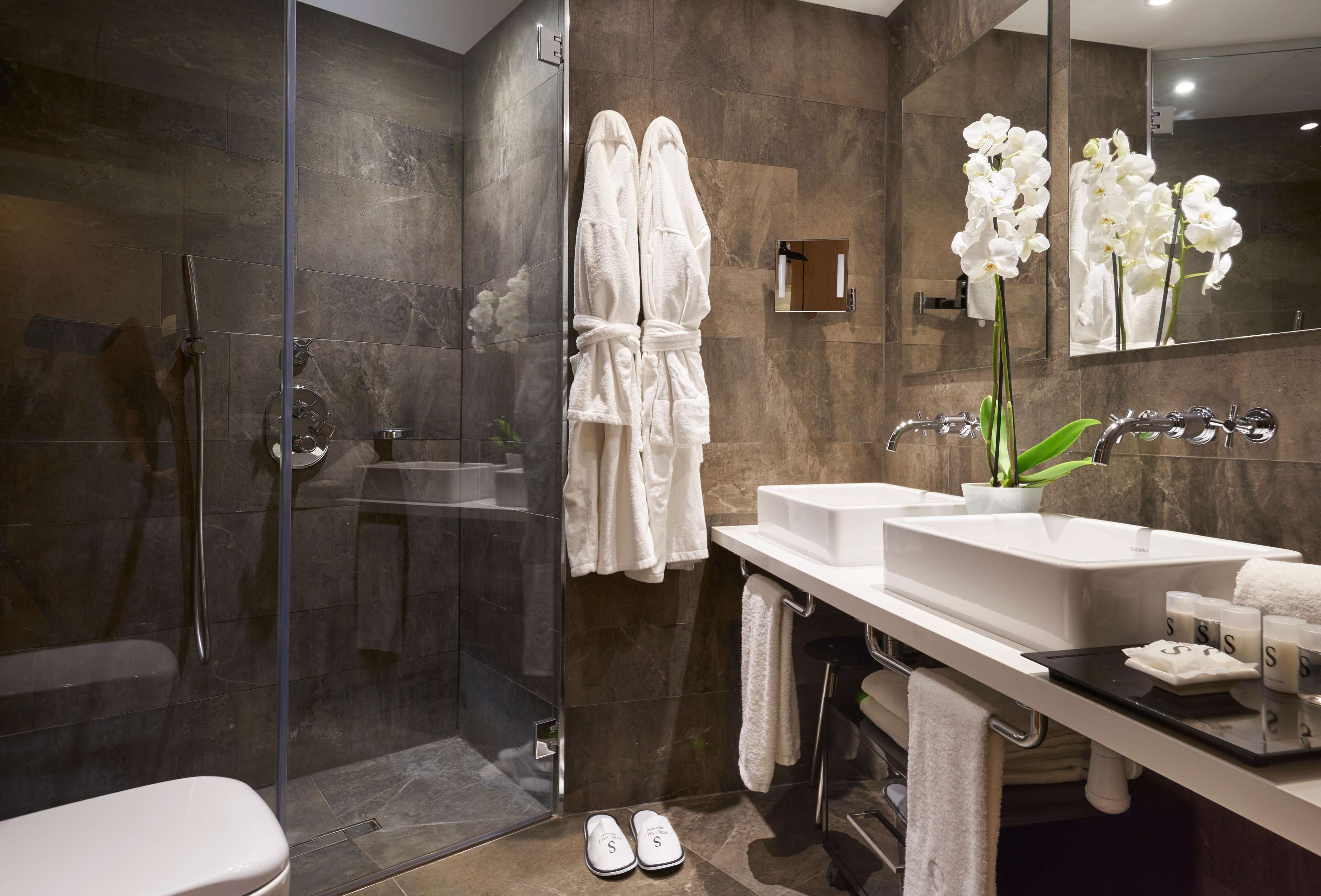 Un baño moderno con cabina de ducha de vidrio, un lavabo blanco y un espejo grande.