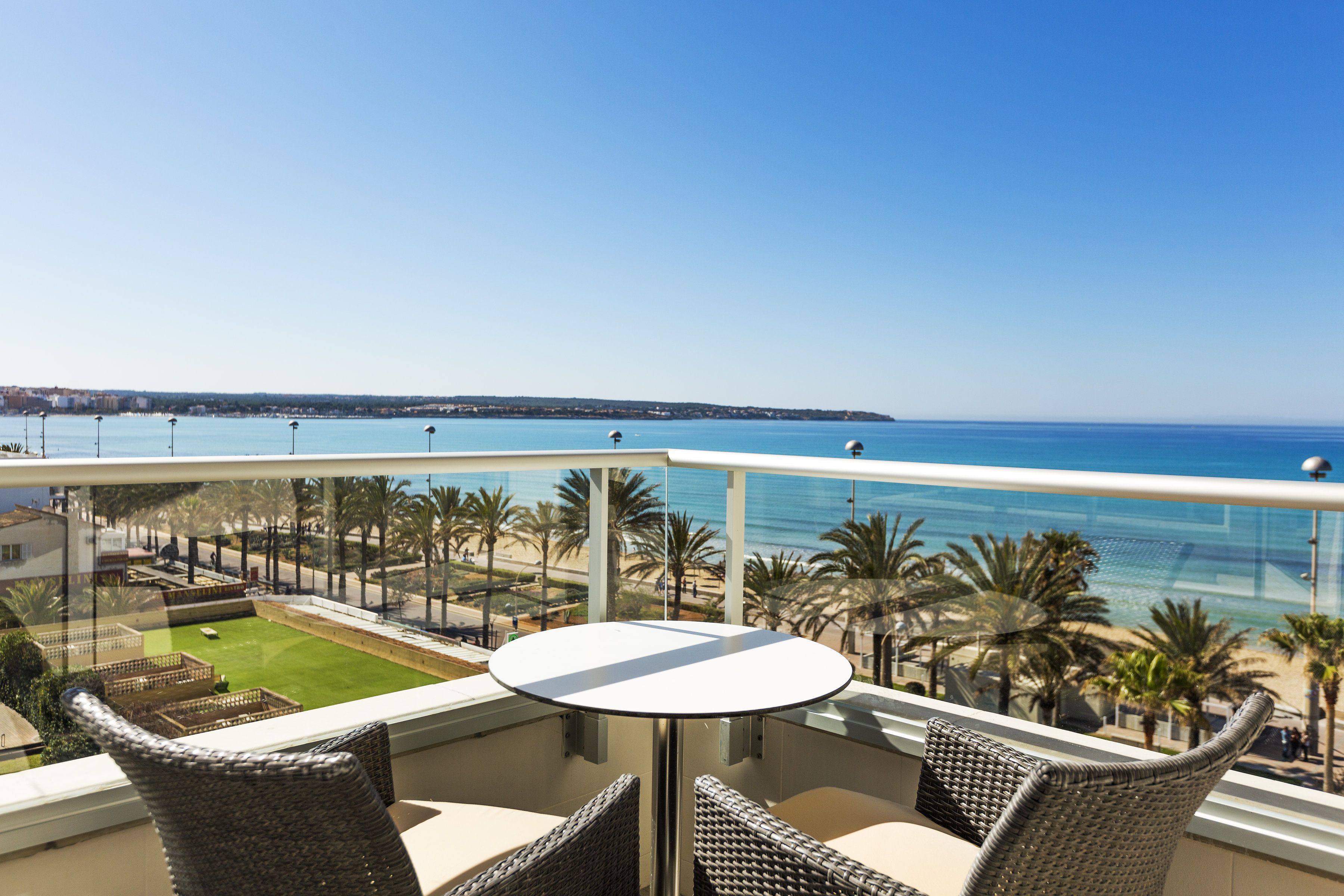 Ein Balkon mit Korbstühlen und einem Tisch, mit Blick auf einen Strand und einen Golfplatz.
