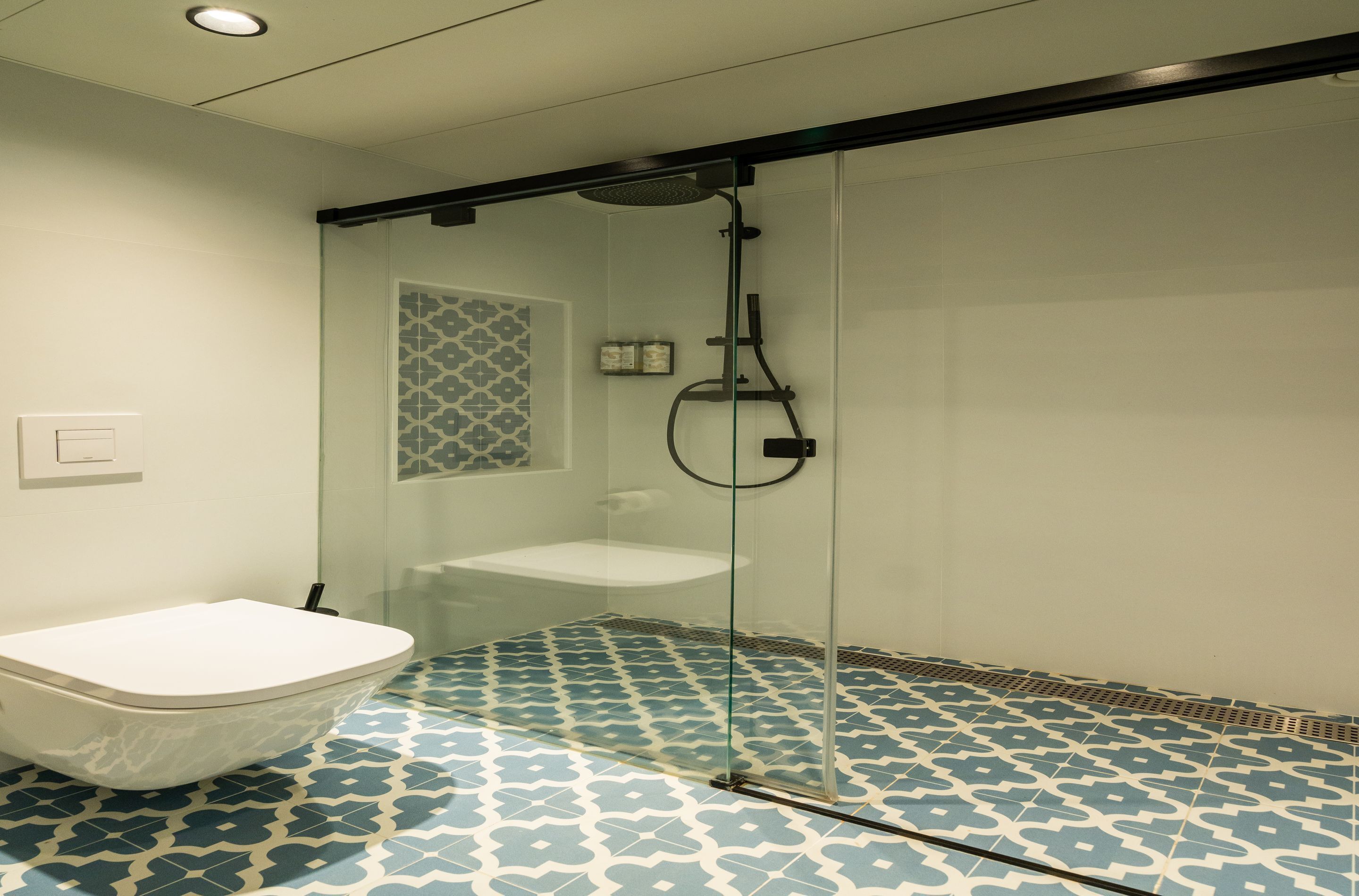 Une salle de bain avec une douche à parois de verre, des toilettes blanches et des carreaux de sol à motifs.