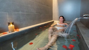 A person relaxing in a bathtub with rose petals and a candle. - Neptuno Hotel & SPA (Calella)