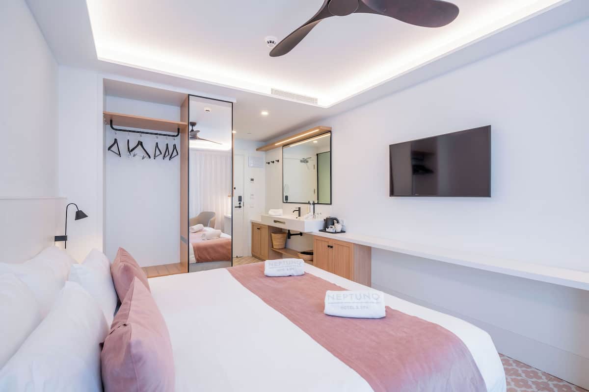 A modern hotel room with a bed, a mirror, a TV, and a bathroom with a shower.