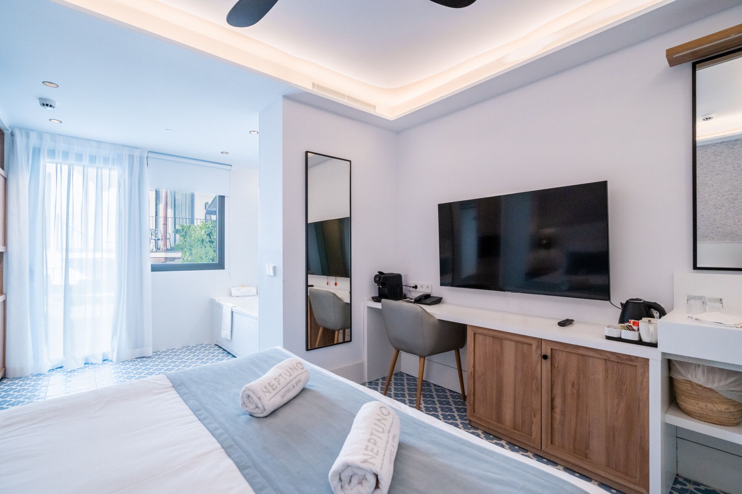 Habitación de hotel moderna con una cama bien hecha, un escritorio con silla, un televisor de pantalla plana y un espejo grande.