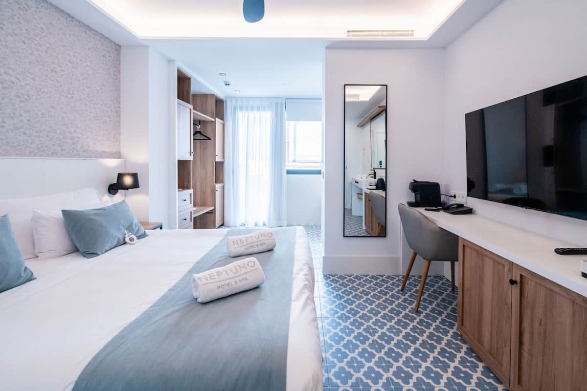 A modern hotel room with a large bed, a desk, a TV, and a bathroom visible through an open door.