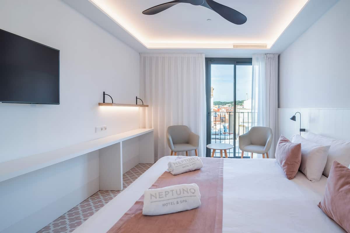 A hotel room with a large bed, a desk, a TV, and a balcony with a view.