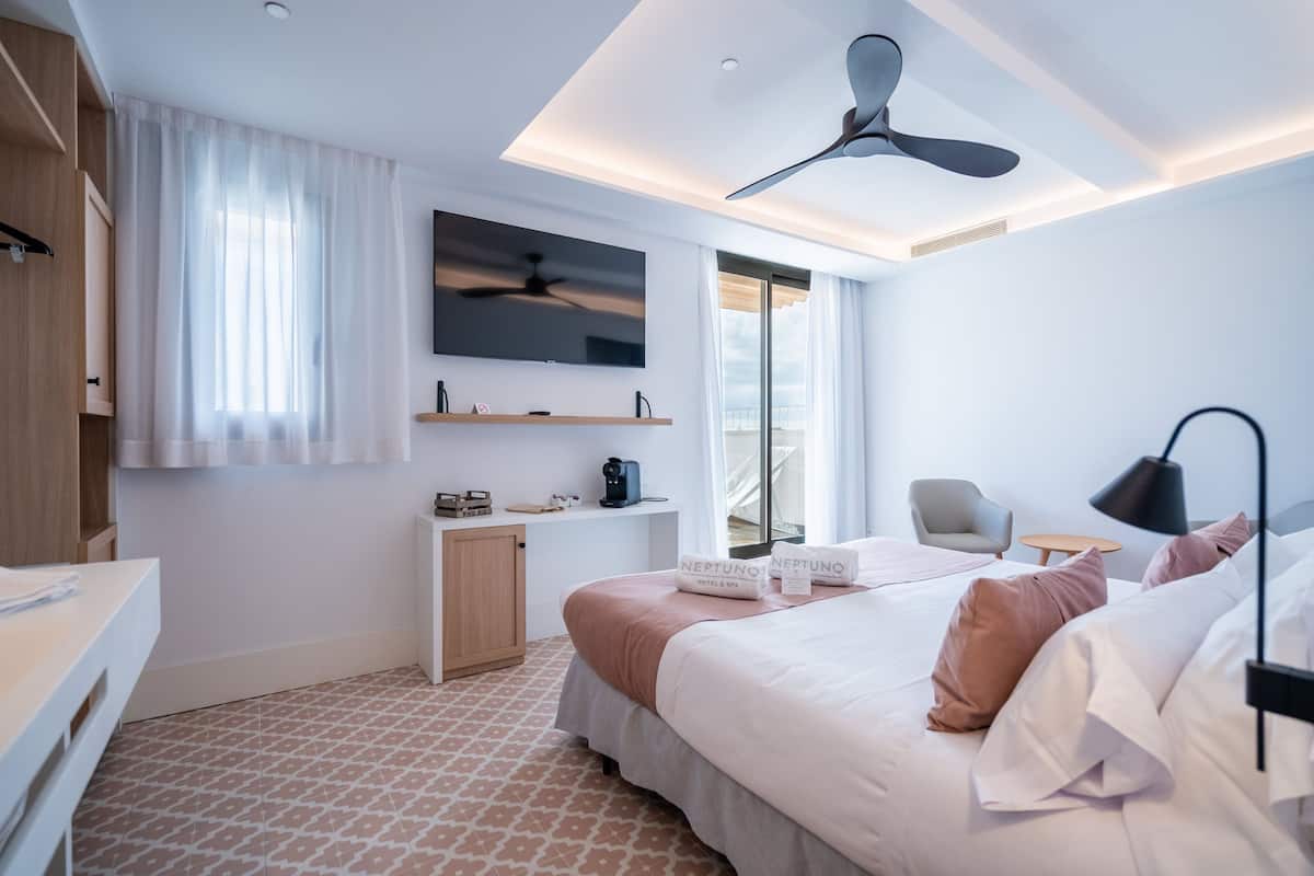 A modern hotel room with a large bed, a ceiling fan, a flat-screen TV, a desk with a chair, and a window with curtains.