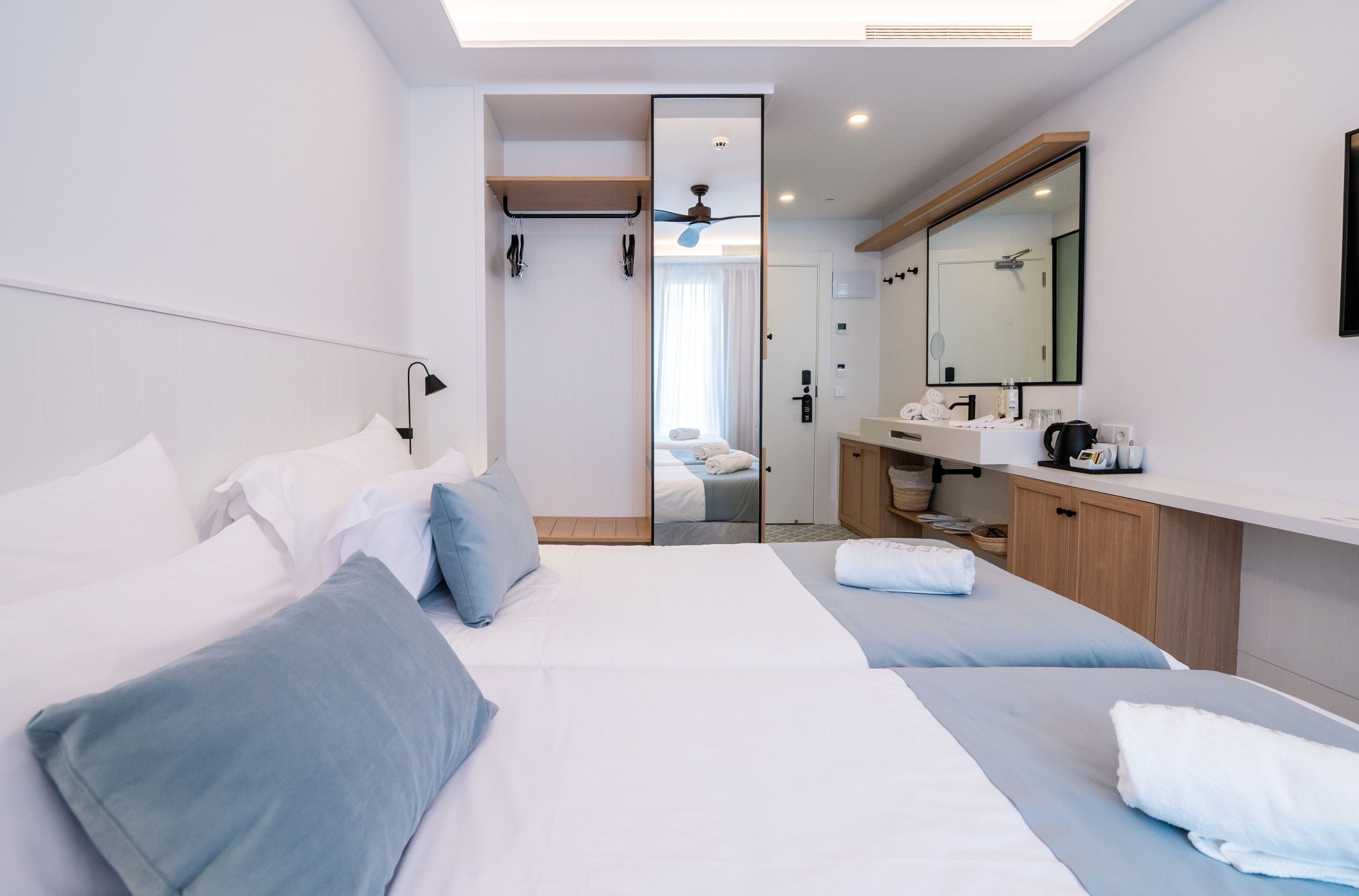 A modern hotel room with a large bed, a separate sitting area, a bathroom with a mirror, and a ceiling fan.