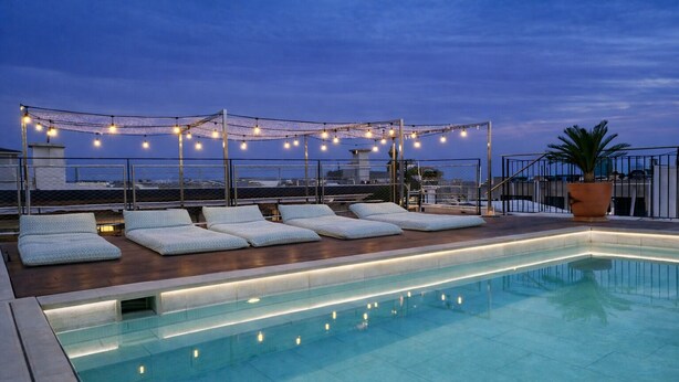 A rooftop pool with lounge chairs and string lights. - Neptuno Hotel & SPA (Calella)