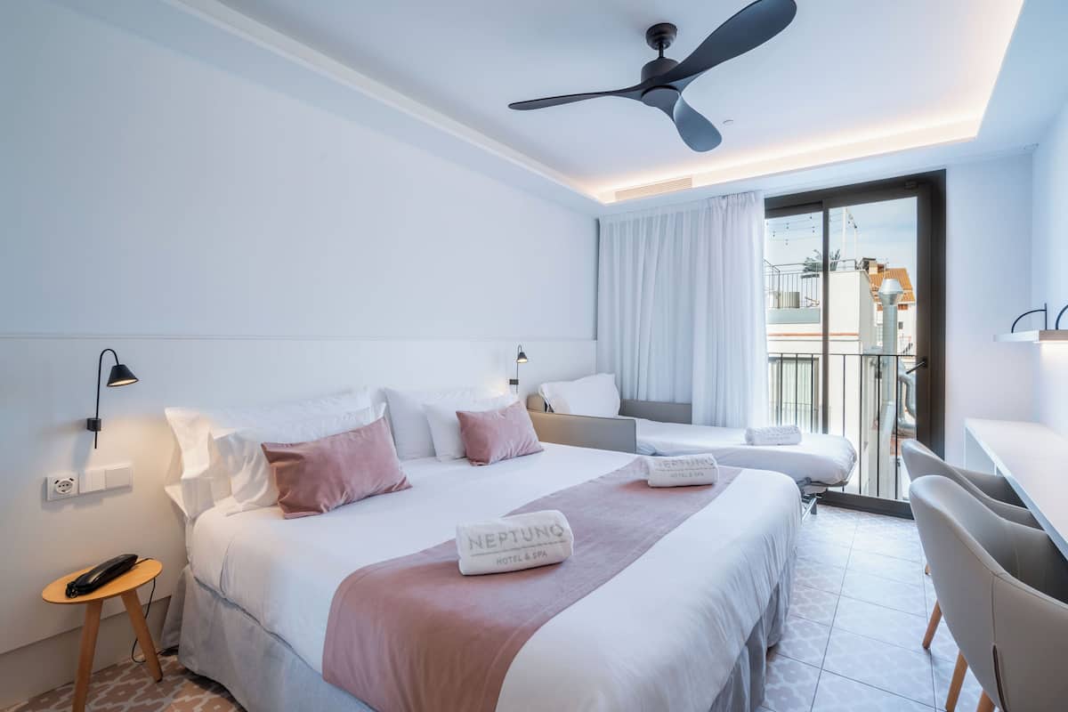 A hotel room with a bed, a desk, a chair, a ceiling fan, and a view of the outside.