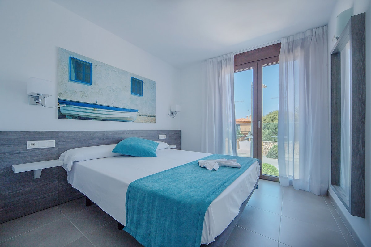 A hotel room with a bed, a window with curtains, a painting on the wall, and a view of the outdoors.