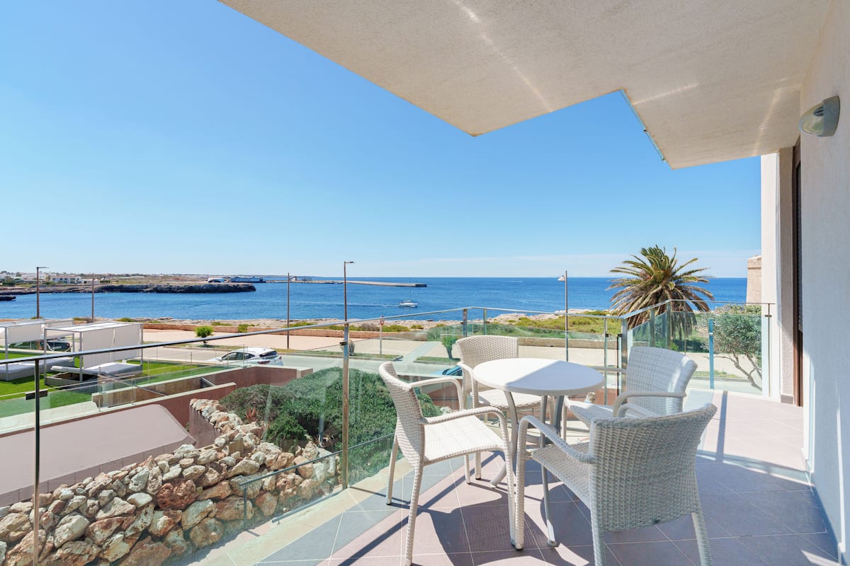 A balcony with a view of the sea, wicker furniture, and a glass railing.