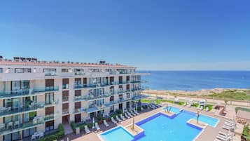 Un hotel de varios pisos con balcones, una zona de piscina y vistas al mar.