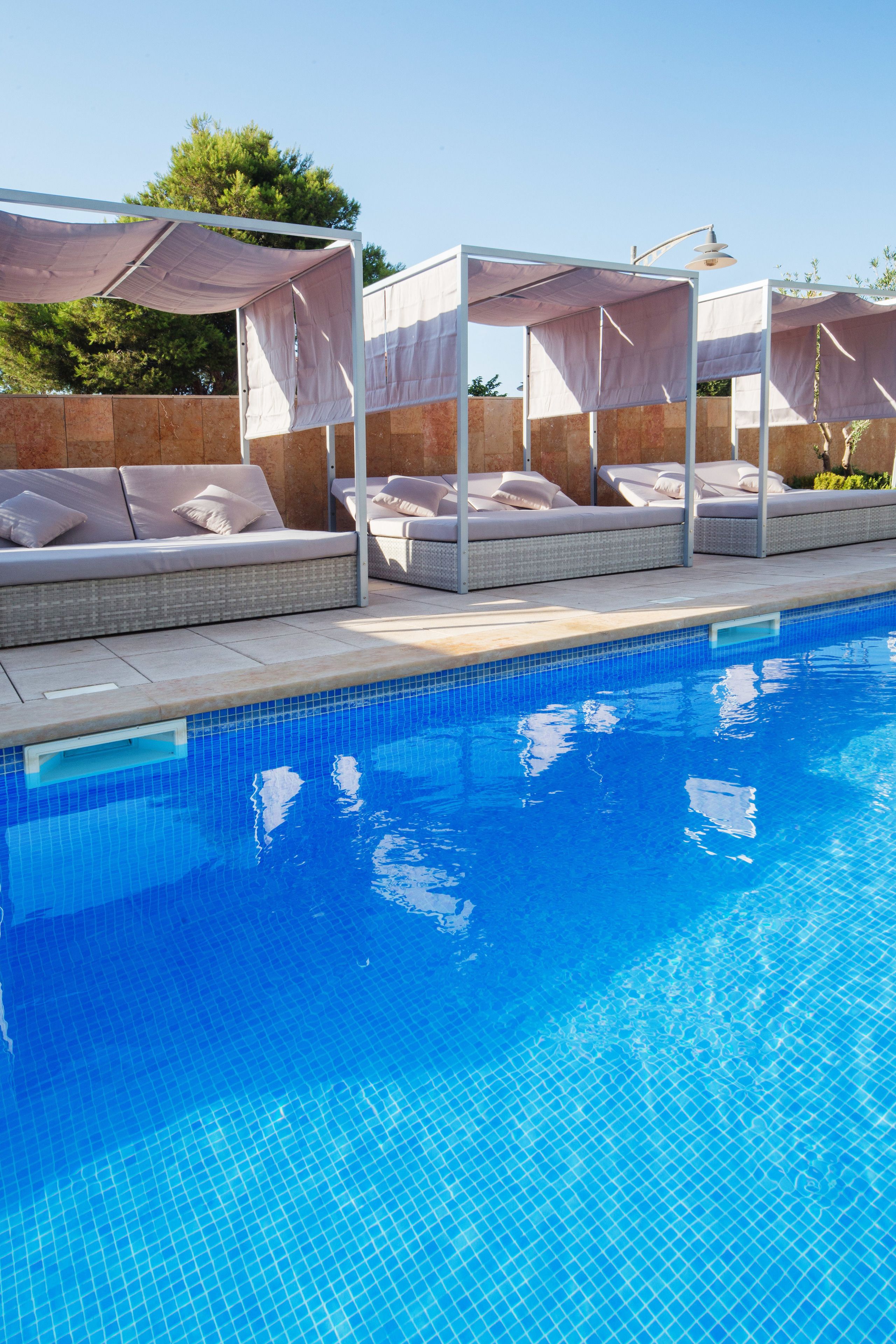 Una piscina con sillones de descanso y toldos.