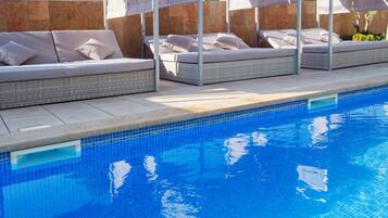 Una piscina con sillones de descanso y toldos.